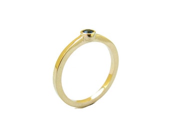 May include: A simple gold band ring with a single, small, dark blue gemstone set in the center.