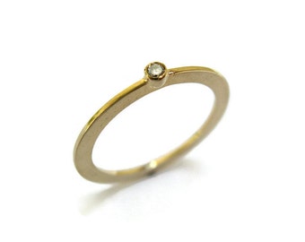 May include: A simple gold band ring with a single small diamond set in the center.