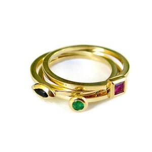 May include: Three gold rings with different coloured gemstones. The top ring has a square ruby, the middle ring has a round emerald, and the bottom ring has a marquise-shaped black stone.