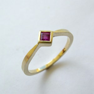 May include: A simple gold band ring with a single square-shaped ruby gemstone set in the center.