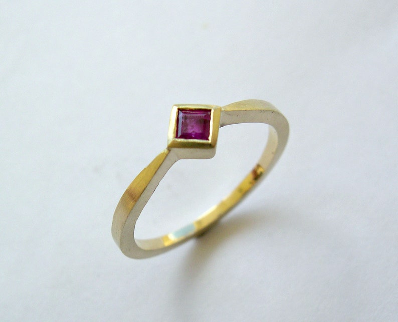 May include: A simple gold band ring with a single square-shaped ruby gemstone set in the center.