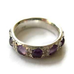 May include: A silver ring with a band of purple gemstones set in a silver filigree design.