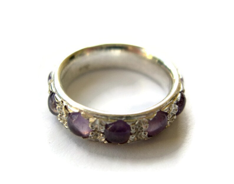 May include: A silver ring with a band of purple gemstones set in a silver filigree design.