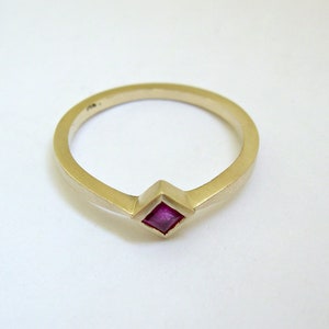 May include: A gold ring with a small, square, pink ruby gemstone set in the center.