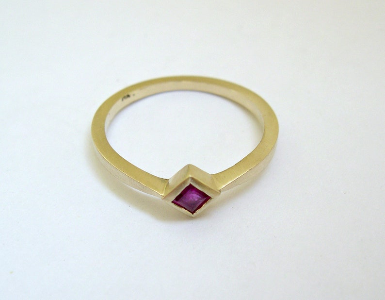 May include: A gold ring with a small, square, pink ruby gemstone set in the center.