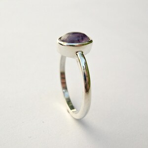 May include: A silver ring with a purple gemstone set in a bezel setting.