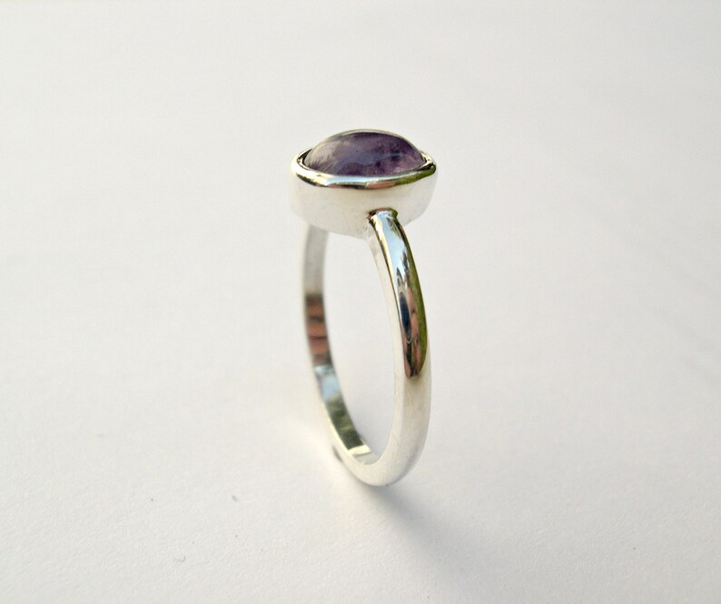 May include: A silver ring with a purple gemstone set in a bezel setting.