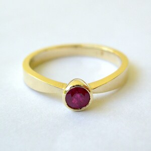 May include: A simple gold band ring with a single round ruby gemstone.