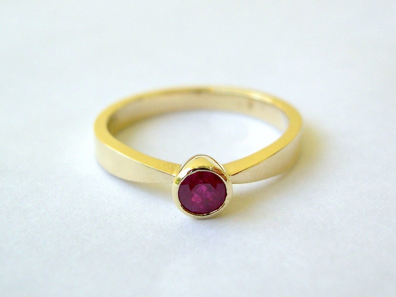 May include: A simple gold band ring with a single round ruby gemstone.