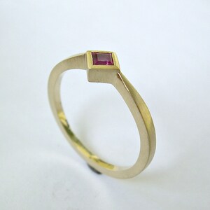 May include: A simple gold band ring with a small square-shaped ruby gemstone set in the center.