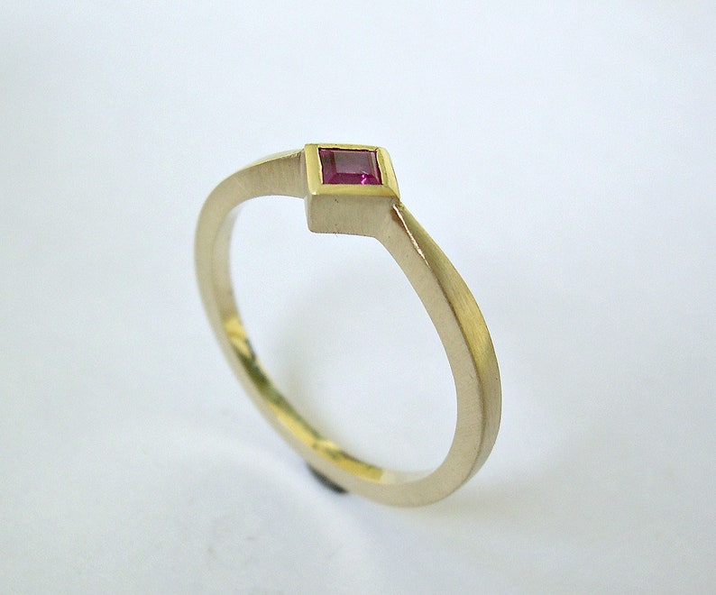 May include: A simple gold band ring with a small square-shaped ruby gemstone set in the center.