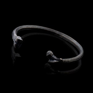 K&ouml;nnte beinhalten: Ein schwarzes Metallarmband mit einem einzigartigen, eckigen Design. Das Armband ist offen und hat einen schlichten, minimalistischen Stil.