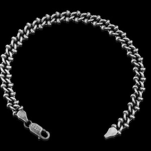 Könnte beinhalten: Ein silberfarbenes Armband mit einem einzigartigen Kettendesign. Die Glieder sind eng gewebt und erzeugen ein strukturiertes Aussehen. Das Armband hat einen Karabinerverschluss. Der Hintergrund ist einfarbig schwarz.