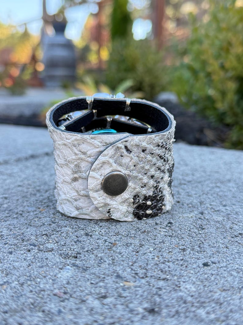 Peut inclure: Un bracelet manchette en cuir blanc et noir &agrave; motif peau de serpent avec une fermeture &agrave; bouton-pression argent&eacute;e. Le bracelet est rempli de divers bijoux argent&eacute;s et turquoise. Un accessoire unique.