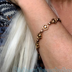 May include: A gold-toned bracelet with a chain link design and round, decorative accents. The bracelet is worn on a person's wrist.