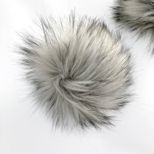 Puede incluir: Un pompón de piel sintética blanco y negro. El pompón es esponjoso y suave.