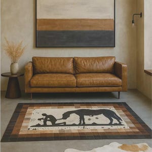 May include: A living room scene featuring a brown leather sofa, a rectangular rug with a horse and rider design, and a cowhide rug. A large abstract painting hangs above the sofa. The room has a neutral color palette with natural light.