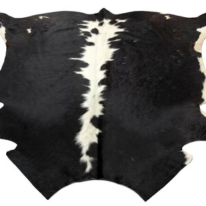 May include: A cowhide rug with a striking black and white pattern. The rug features a large expanse of black with a prominent white stripe running down the centre. The edges are irregularly shaped, adding to its natural aesthetic.