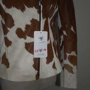 Pode incluir: Casaco de pele de vaca castanho e branco com fecho de correr. O casaco tem uma etiqueta de tamanho m&eacute;dio. O casaco &eacute; exibido num manequim.