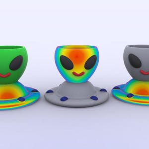 May include: Three alien-shaped egg cups with a rainbow-colored base. The egg cups are green, orange, and gray.