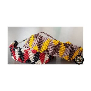 Puede incluir: Dos pulseras de la amistad hechas con hilo de bordar de colores. Una pulsera es marrón, amarilla y morada. La otra pulsera es negra, roja y blanca. Las pulseras están atadas juntas y el texto "Manu Kon Arte" es visible en la esquina inferior derecha de la imagen.