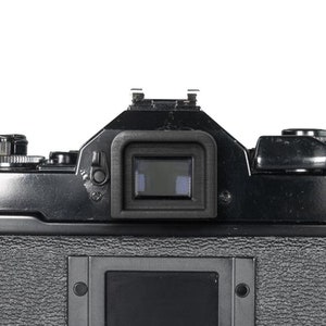 Peut inclure: Un appareil photo argentique noir avec un viseur et un panneau arrière à surface texturée.