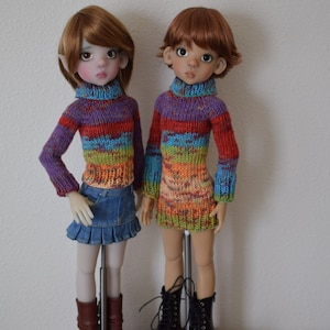Puede incluir: Dos muñecas con suéteres de rayas de colores y botas. Una muñeca lleva una falda vaquera. Las muñecas están de pie sobre bases de madera.