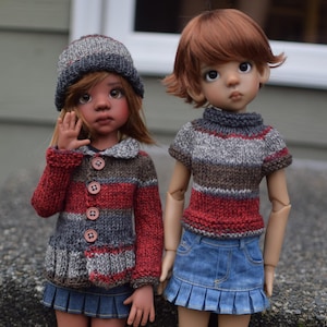 Könnte beinhalten: Zwei Puppen, die gestrickte Pullover und Röcke tragen. Die Puppe links trägt einen grau-rot gestreiften Pullover mit einer grauen Mütze. Die Puppe rechts trägt einen braun-grau-rot gestreiften Pullover mit einem Jeansrock.