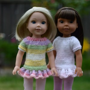 Peut inclure: Deux poupées portant des robes tricotées. Une poupée a les cheveux blonds et porte une robe rayée avec un volant rose. L'autre poupée a les cheveux bruns et porte une robe blanche avec un volant blanc.