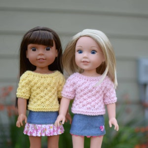 May include: Two dolls wearing knitted sweaters and denim skirts. The doll on the left has brown hair and is wearing a yellow sweater. The doll on the right has blonde hair and is wearing a pink sweater.