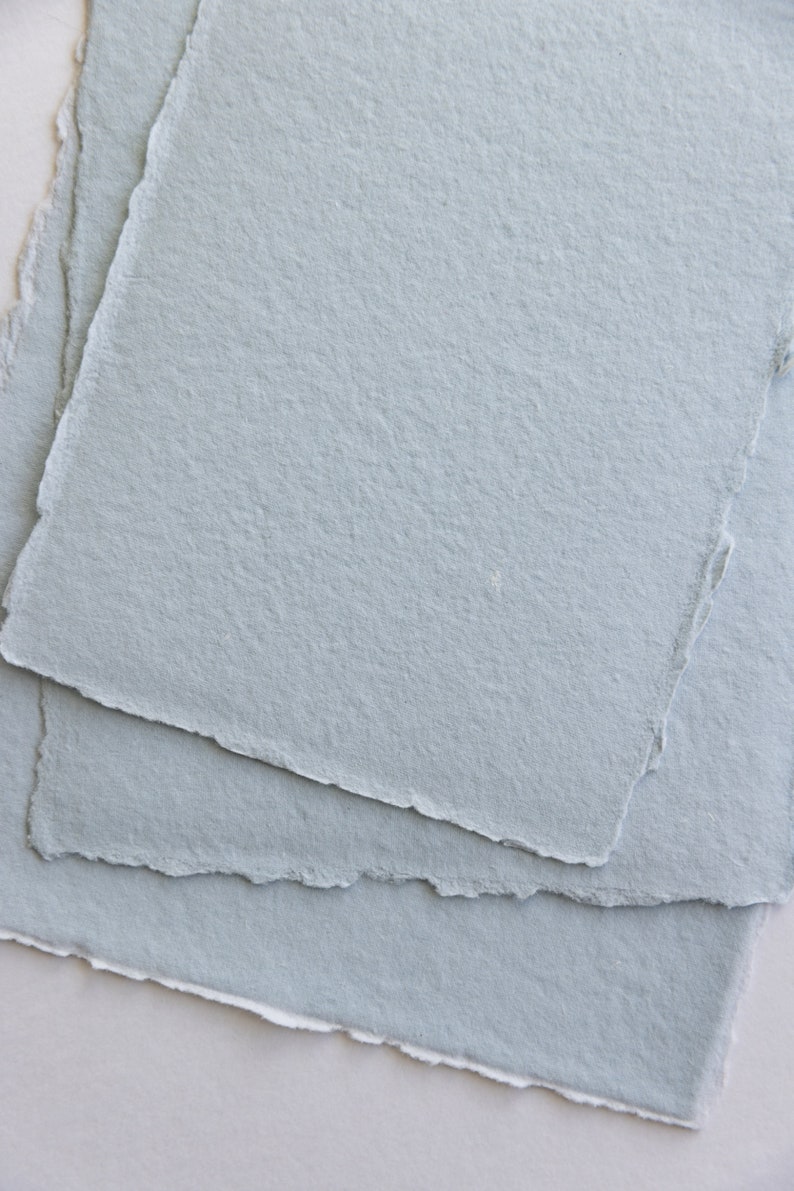 Puede incluir: Pila de tres hojas de papel texturizado azul claro con bordes irregulares.