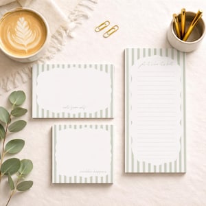 Puede incluir: Una composición plana con artículos de papelería. Hay tres blocs de notas con borde festoneado y un patrón de rayas en verde claro y blanco. Los blocs de notas tienen el texto "note from self", "scribble happens" y "get it like it's hot".
