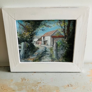 May include: A framed painting depicting a white farmhouse with a red roof, surrounded by trees and a dirt path leading to the front door.