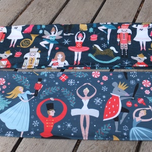 May include: Two fabric panels with a Nutcracker theme. The top panel features a dark blue background with white, red, and gold Nutcracker characters, ballerinas, and other festive elements. The bottom panel features a dark blue background with a white, red, and gold Nutcracker theme with ballerinas, a mouse king, and a Christmas tree.