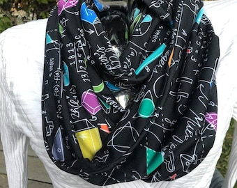 Op de afbeelding: Een zwarte oneindigheidssjaal met een witte en kleurrijke print van wiskundige vergelijkingen en symbolen. De sjaal is gemaakt van een zachte, rekbare stof en is perfect om een ​​persoonlijke touch aan elke outfit toe te voegen.