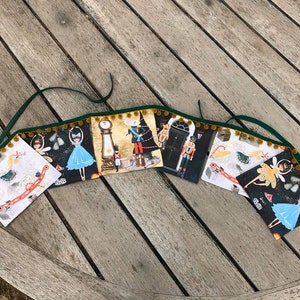 Puede incluir: Una pancarta navideña festiva con seis paneles coloridos que presentan ilustraciones de una bailarina, un reloj, un cascanueces, un caballo de balancín, un hada y un copo de nieve. La pancarta está decorada con una cinta verde y pompones dorados.