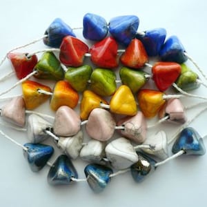 Peut inclure: Un ensemble de perles triangulaires colorées enfilées sur un cordon blanc. Les perles sont dans les tons de rouge, orange, jaune, vert, bleu, rose et gris. Les perles ont une finition brillante et sont disposées en cercle.