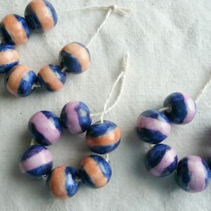 Peut inclure: Trois brins de perles, chacun avec des rayures bleues et roses alternées. Les perles sont enfilées sur une ficelle blanche.