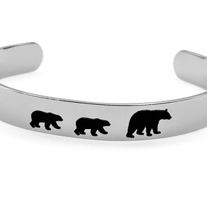 May include: A silver bracelet with a design of three black bears walking in a line. The bears are cut out of the metal and the design is on a silver band.