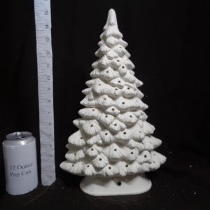 May include: A white ceramic Christmas tree with a textured surface and a base. The tree is approximately 10 inches tall. A 12-ounce pop can is next to the tree for size comparison. The tree has small holes for lights.