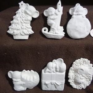 May include: Set of eight white ceramic Christmas ornaments featuring a mouse theme. The ornaments depict a mouse holding a Christmas tree, a mouse riding a sleigh, a mouse holding a stocking, a mouse sleeping on a present, a mouse holding a wreath, a mouse holding a bell, a mouse holding a candy cane, and a mouse holding a star.
