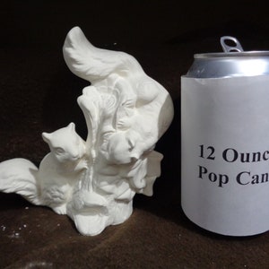 May include: White ceramic figurine of two squirrels on a tree trunk. The figurine is approximately the size of a 12-ounce pop can.