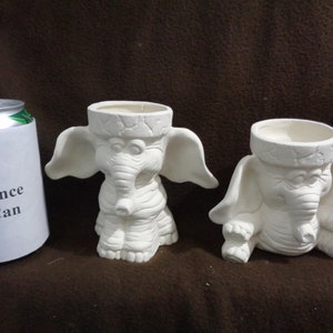 May include: Two white ceramic elephant planters, each with a 12 ounce pop can for size reference. The planters are in the shape of an elephant with large ears and a trunk.