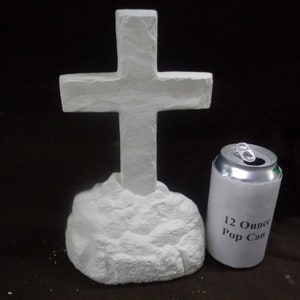 May include: White ceramic cross on a rock base, next to a 12-ounce pop can for size comparison. The cross is approximately 12 inches tall.