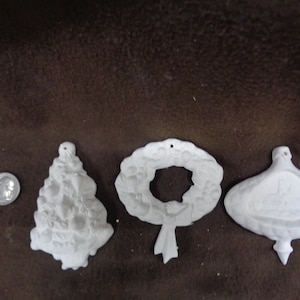 May include: Set of four white ceramic Christmas ornaments. The ornaments are shaped like a Christmas tree, a wreath, a bell, and a star. The ornaments are ready to be painted.