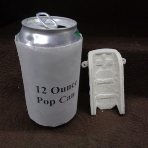 May include: A white plaster mold for making a 12 ounce pop can. The mold is next to a 12 ounce pop can with a white paper sleeve that says "12 Ounce Pop Can".