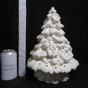 May include: A white ceramic Christmas tree with a textured surface. The tree is approximately 12 inches tall. A 12-ounce pop can is next to the tree for size comparison. The tree has small holes for lights.