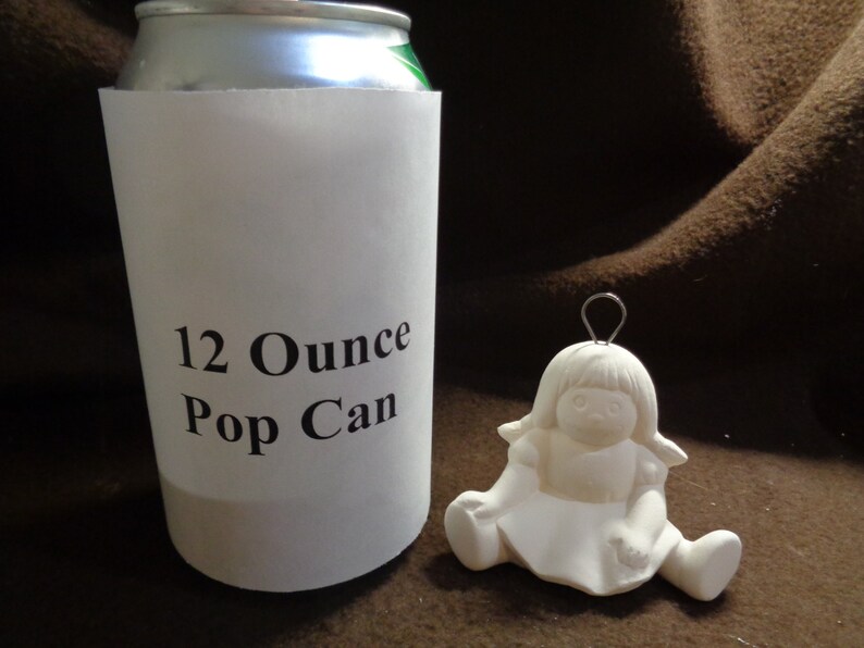May include: A white ceramic figurine of a girl sitting with her legs crossed. The figurine is 12 ounces and is the size of a standard pop can. The figurine has a wire loop on the top of her head for hanging.