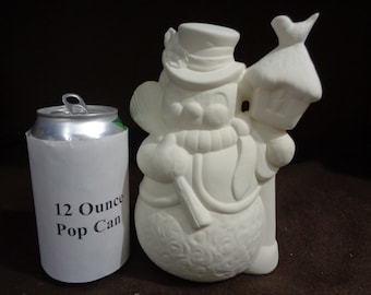 May include: White ceramic snowman figurine holding a stick and standing next to a white ceramic birdhouse. The snowman is wearing a hat and scarf. The figurine is approximately 12 ounces, as indicated by the pop can in the image.