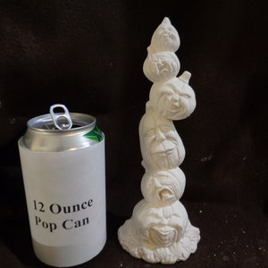 May include: A white ceramic sculpture of five stacked pumpkins with carved faces. The sculpture is approximately the size of a 12-ounce pop can.